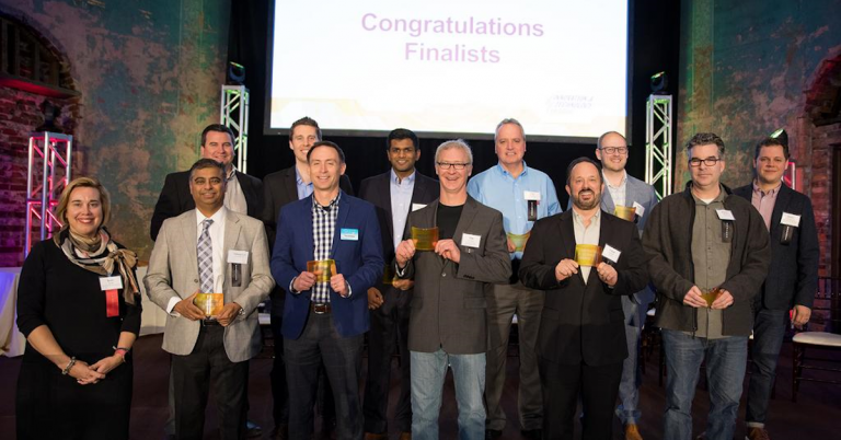 Group of award finalists standing on stage at an awards ceremony beneath a Congratulations Finalists screen