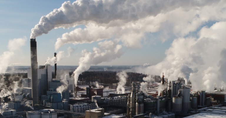 Paper mill emitting steam plumes from its stacks beside a waterway