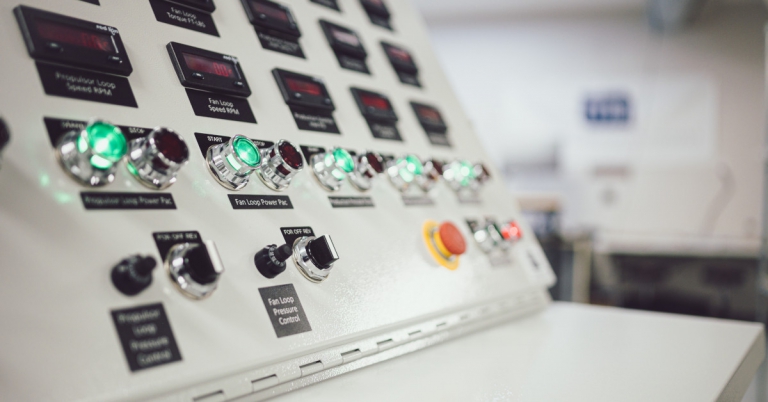 Close-up of an industrial control panel with illuminated push-buttons and indicator gauges