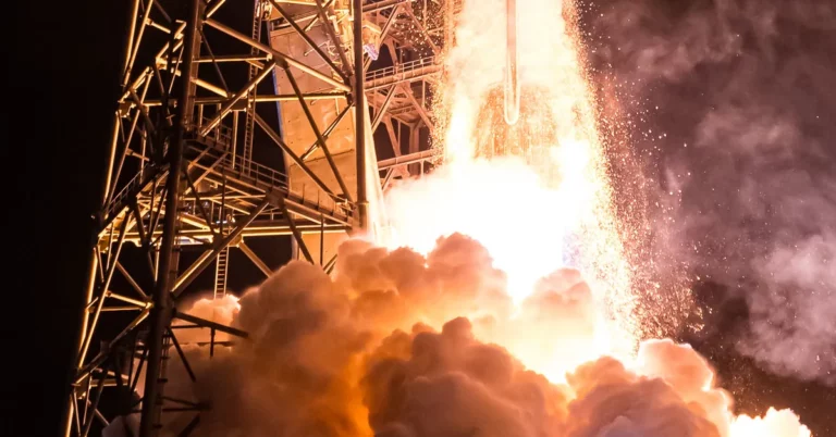 Close-up of a rocket launch at night with bright flames, smoke, and a launch tower.